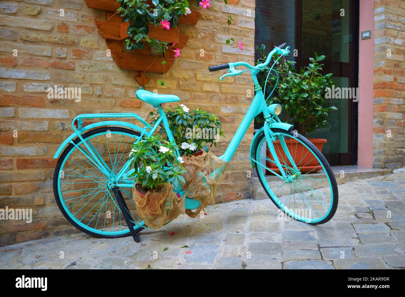 Vecchia bicicletta con fiori nel cesto di fronte ad un muro di mattoni a Recanati, Italia Foto Stock