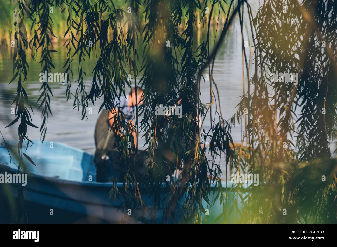 Pescatori sfocati in barca dietro rami salici appesi Foto Stock