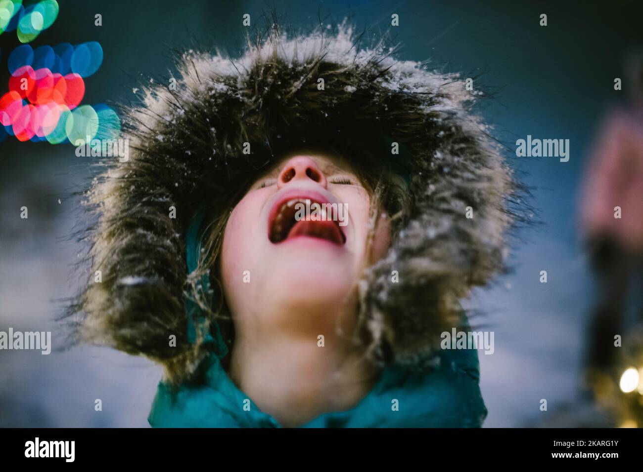 La ragazza cattura la neve sul cappotto di pelliccia e in bocca durante la tempesta di neve d'inverno Foto Stock