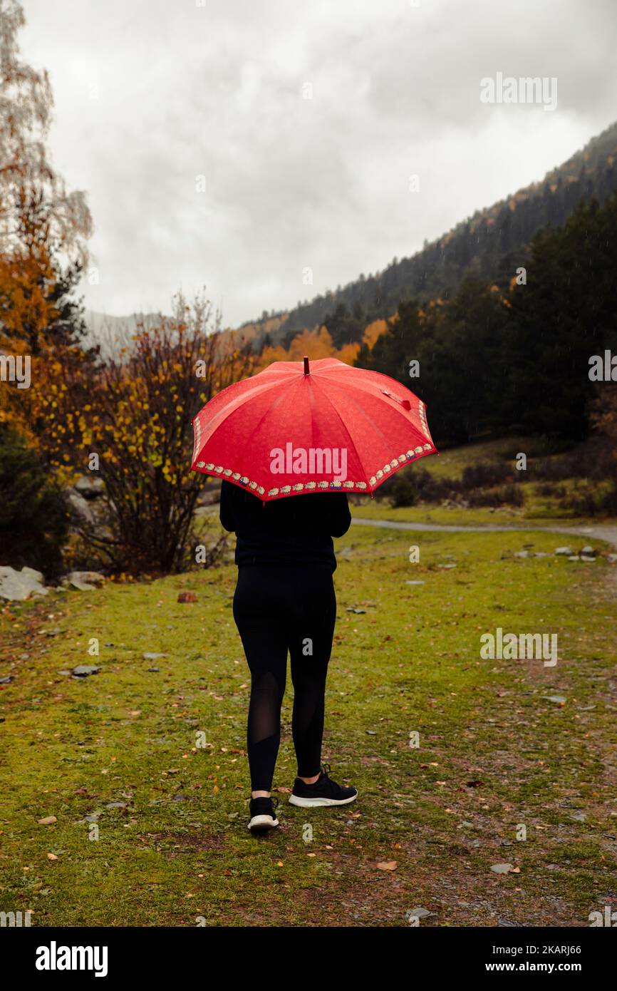 Ragazza con un ombrello rosso che fa un percorso attraverso la montagna Foto Stock