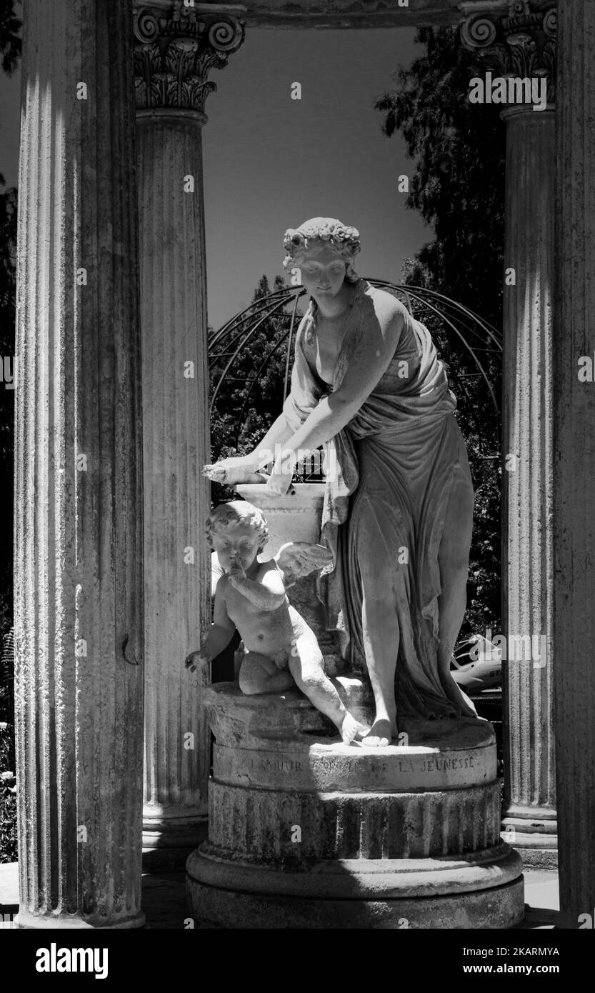 Uno scatto verticale bianco e nero di una statua di una donna e di un angelo all'aperto vicino a una fontana d'acqua Foto Stock Uno scatto verticale bianco e nero di una statua di una donna e di un angelo all'aperto vicino a una fontana d'acqua Foto Stock