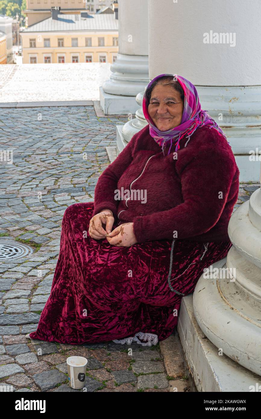 Helsinki, Finlandia - 19 luglio 2022: Primo piano di colore, viola, rosa, rosso vestito, più vecchio, Sorridente signora Gipsy che prega all'ingresso della Cattedrale. Solo Foto Stock