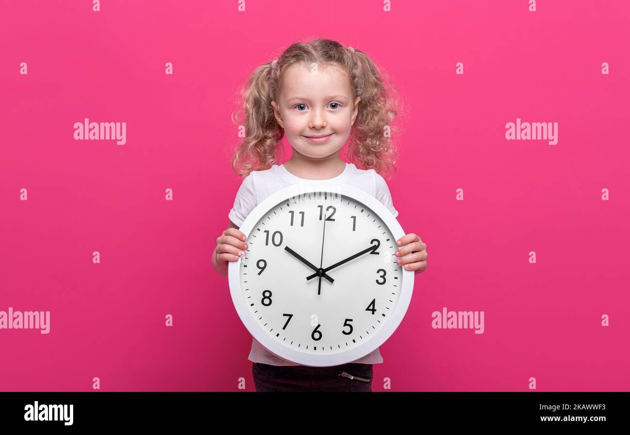 Una bambina tiene un orologio bianco su uno sfondo rosa. Foto Stock