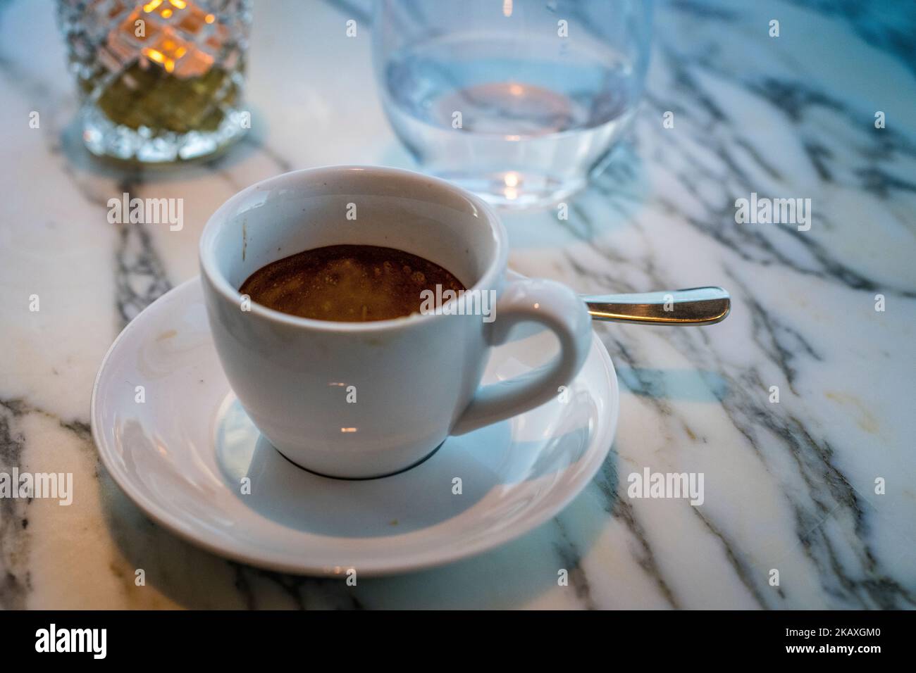 Chiudete il caffè espresso in tazza con un bicchiere d'acqua e uno sfondo e una luce del tè che si illumina su un tavolo di marmo. Foto Stock