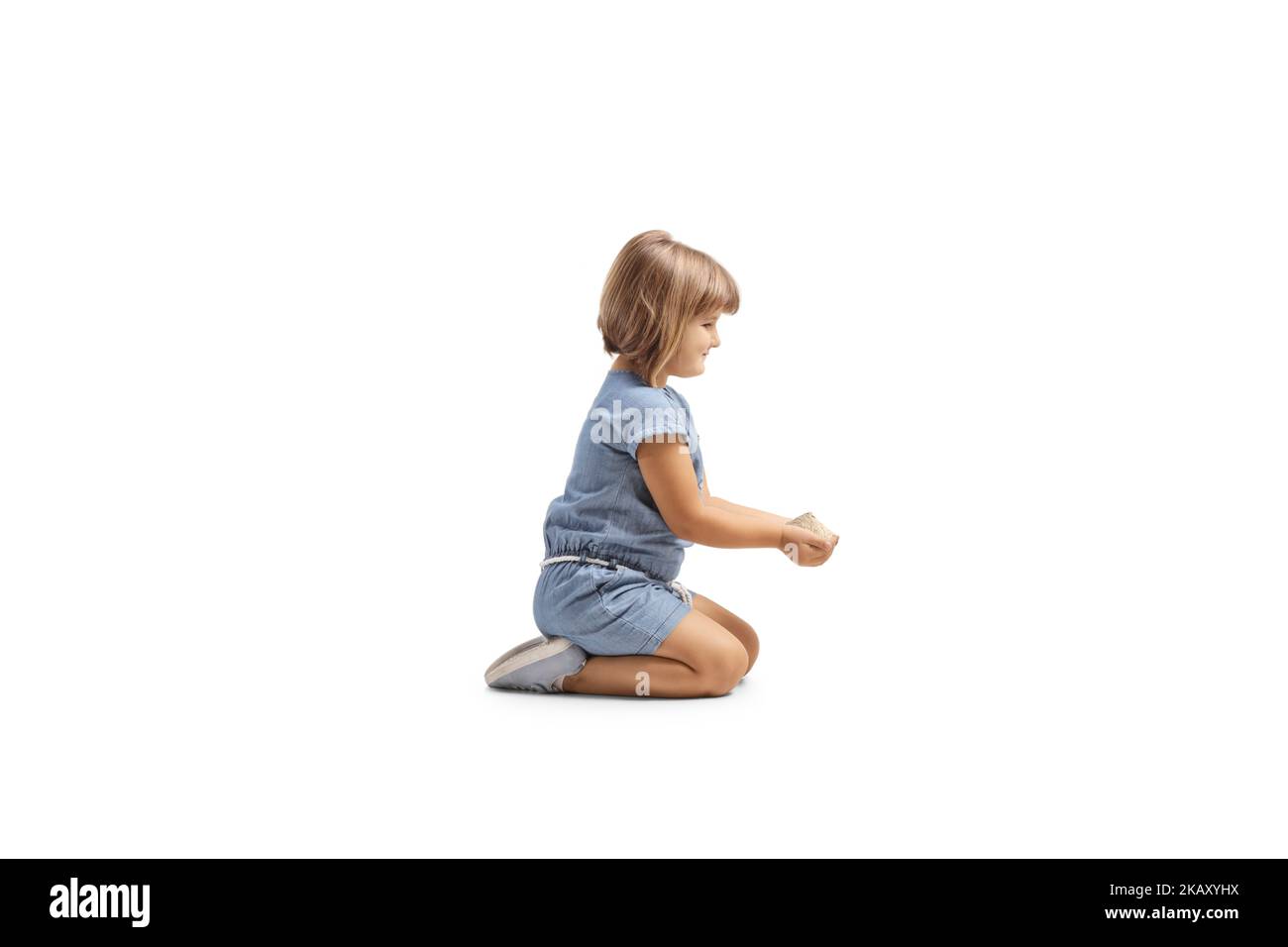 Profilo shot di una bambina che tiene cibo in grano nelle sue mani e inginocchiandosi isolato su sfondo bianco Foto Stock