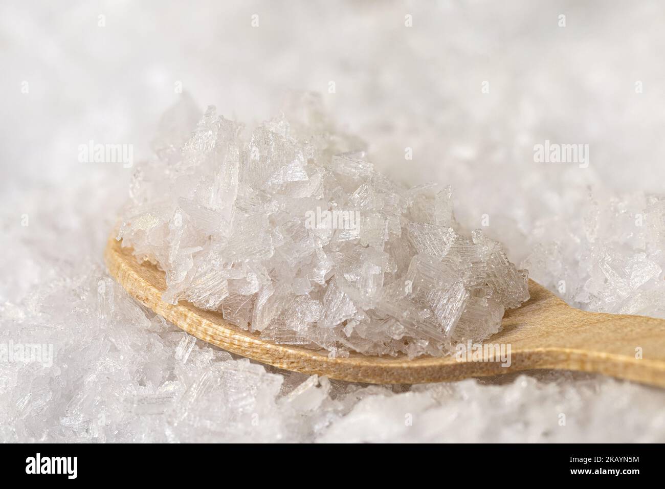 Scaglie di sale marino su cucchiaio di legno su fondo di sale marino. Foto Stock