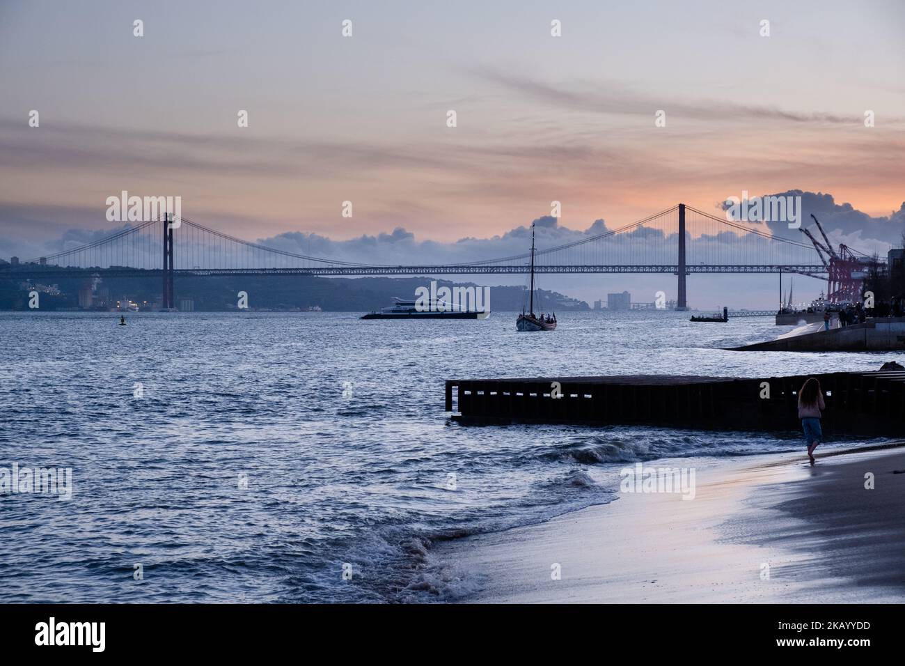 SERATA A LISBONA: Viste del Ponte 25 de Abril e del Santuário de Cristo Rei sulla passeggiata Tejo lungo la spiaggia e le onde del fiume Tago (Rio Tejo) Foto Stock