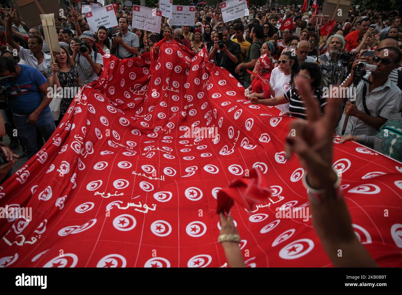 Le donne sventolano una gigantesca bandiera tunisina e firmano la vittoria durante la celebrazione della Giornata Nazionale della Donna in avenue Habib Bourguiba a Tunisi, Tunisia, il 13 agosto 2018. I manifestanti hanno chiesto la parità di genere, la parità di successione per le donne, i diritti delle LGBT e i diritti delle donne tunisine. I manifestanti hanno protestato anche contro il partito islamico Ennahda e hanno espresso il loro sostegno al Comitato per le libertà individuali e l'uguaglianza (COLIBE). All'inizio della giornata, il presidente tunisino Beji Caid Essebsi ha annunciato che il disegno di legge sulla parità di successione per le donne sarà presentato all'Assemblea della Rep Foto Stock