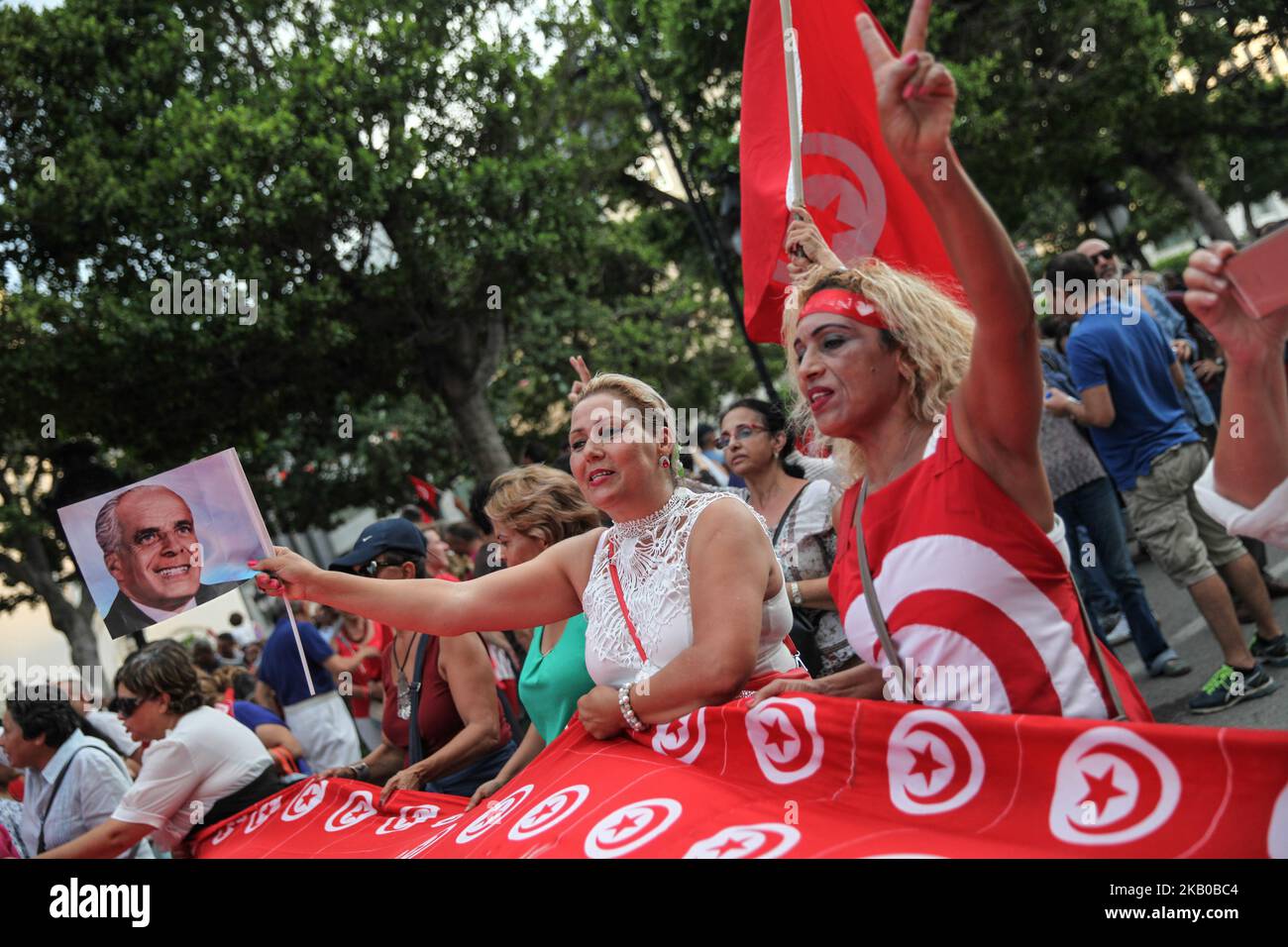 Una donna che indossa la bandiera tunisina fa il segno della vittoria, mentre un’altra donna emana un’aporiadel precedente presidente tunisino, Habib Bourguiba, durante la celebrazione della Giornata Nazionale della Donna in Avenue Habib Bourguiba a Tunisi, Tunisia, il 13 agosto 2018. I manifestanti hanno chiesto la parità di genere, la parità di successione per le donne, i diritti delle LGBT e i diritti delle donne tunisine. I manifestanti hanno protestato anche contro il partito islamico Ennahda e hanno espresso il loro sostegno al Comitato per le libertà individuali e l'uguaglianza (COLIBE). All’inizio della giornata, il presidente tunisino, Beji Coid Essebsi, ha annunciato che il disegno di legge o Foto Stock