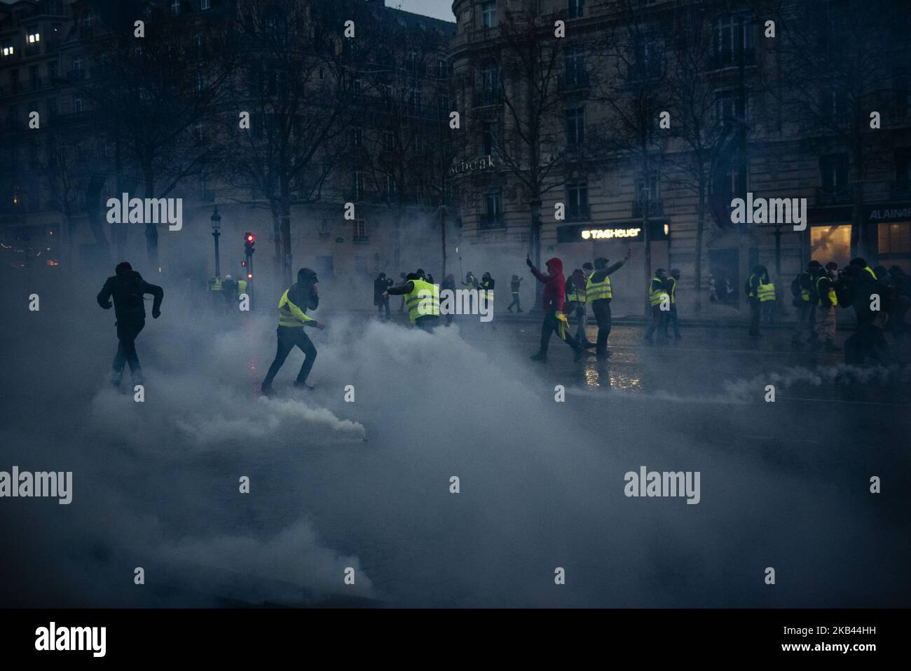 I manifestanti si proteggono mentre si riempiono gas lacrimogeni vicino agli Champs Elysees Avenue a Parigi, in Francia, il 15 dicembre 2018. Nonostante i ministri del governo francese si appellino alle proteste a livello nazionale dei Gilets Jaunes (gilet giallo) per fermarsi a seguito dell'attacco di Strasburgo che ha ucciso tre persone il 11 dicembre, i manifestanti hanno preso le strade della Francia per il quinto sabato consecutivo. Il movimento 'Gilets Jaunes' ('Yellow Vest') - iniziato il 17 novembre 2018 e ispirato dall'opposizione ad una nuova tassa sui carburanti - ha assorbito un'ampia gamma di sentimenti anti-governativi e distrutto Parigi e altre città francesi Foto Stock