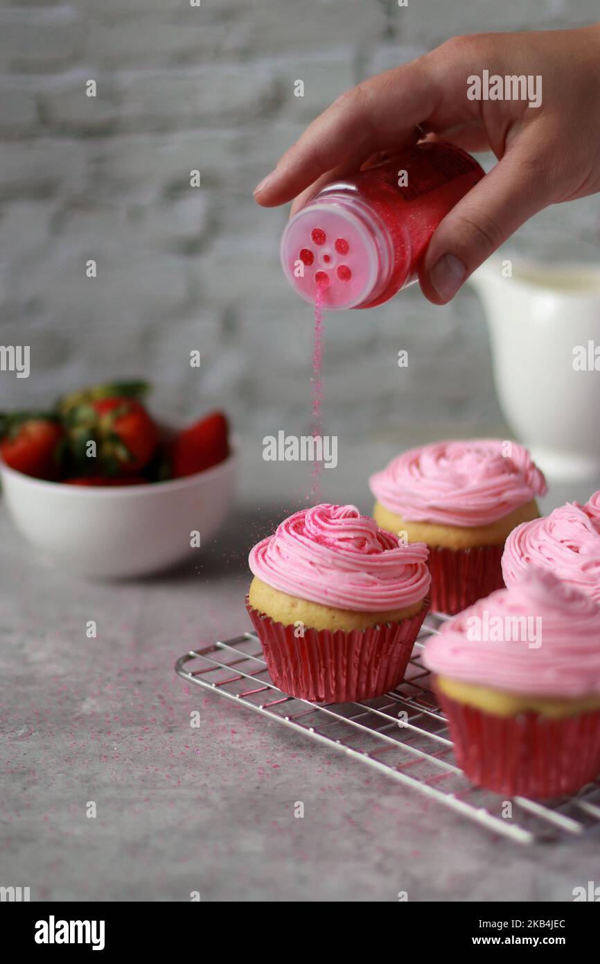 Le paillette a mano rosa cospargono i muffin con la crema di fragole gelata sulla parte superiore Foto Stock