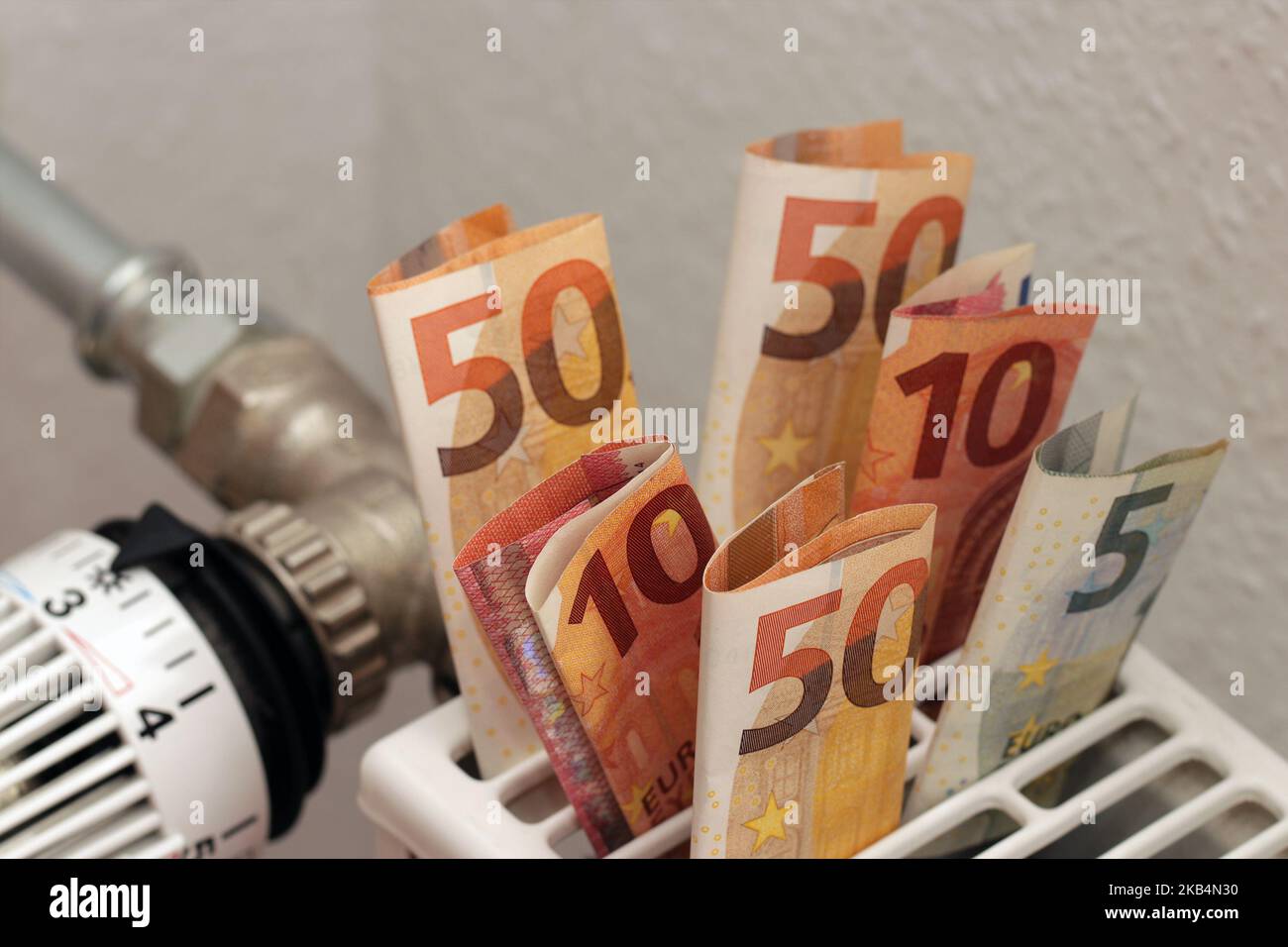 Banconote di carta euro inserite nel radiatore di riscaldamento a casa. Un simbolo dell'aumento dei costi di riscaldamento. Soldi per pagare le fatture. Foto Stock