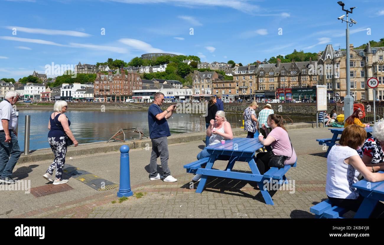 Turisti che si godono il tempo estivo su Oban Quay con Oban sullo sfondo Foto Stock