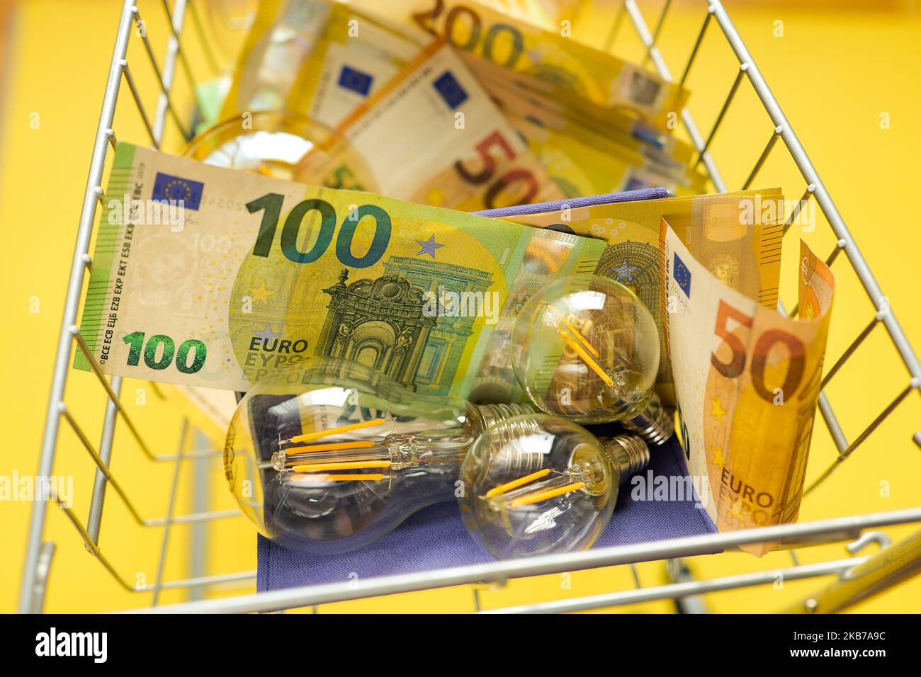 Costi dell'elettricità.lampadine leggere e banconote in euro in un carrello supermercato su sfondo giallo.crisi nel settore dell'energia.pagamento dell'elettricità Foto Stock