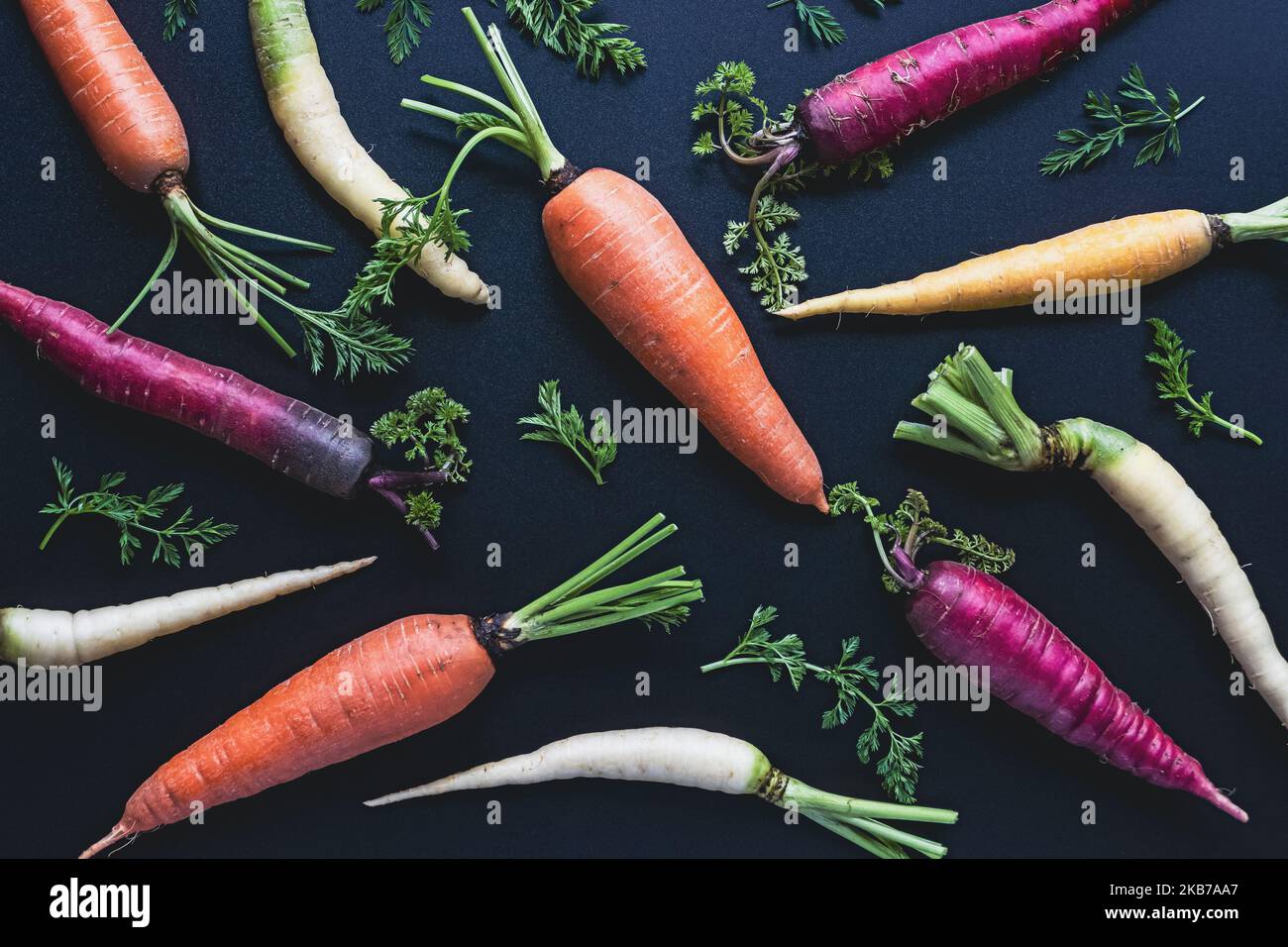 Motivo di carote colorate su sfondo nero, giacitura piatta di carote arcobaleno, vista dall'alto Foto Stock