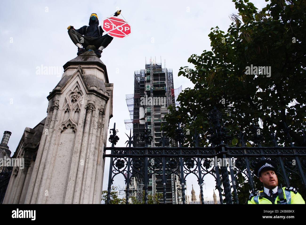 Un membro del movimento attivista per il cambiamento climatico Extinction Rebellion (XR), indossando una maschera a gas e circondato dalla polizia, si è mostrato in cima al muro del Parliament Estate a Londra, in Inghilterra, il 15 ottobre 2019. XR ha promesso di continuare la sua ribellione di due settimane in città, nonostante la polizia metropolitana, la scorsa notte, che ha emesso un divieto di azioni di protesta da parte del gruppo, e ha eliminato il suo accampamento in Trafalgar Square. (Foto di David Cliff/NurPhoto) Foto Stock