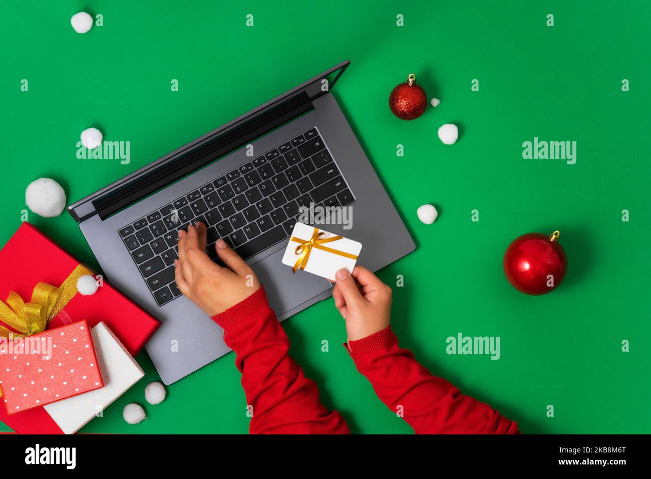 Vista dall'alto del laptop e delle mani della donna che inseriscono i dettagli della carta per il pagamento, sfondo verde decorazione natalizia. Piatto sfondo laico per la promozione di Christm Foto Stock