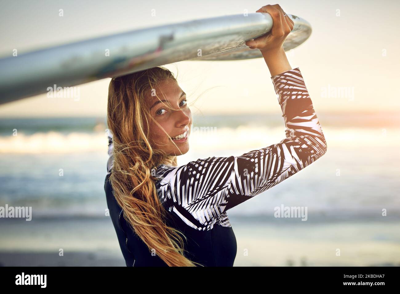 Unisciti a me. Ritratto retroverso di una giovane e attraente surfista in piedi con la sua tavola da surf che guarda sopra l'oceano. Foto Stock