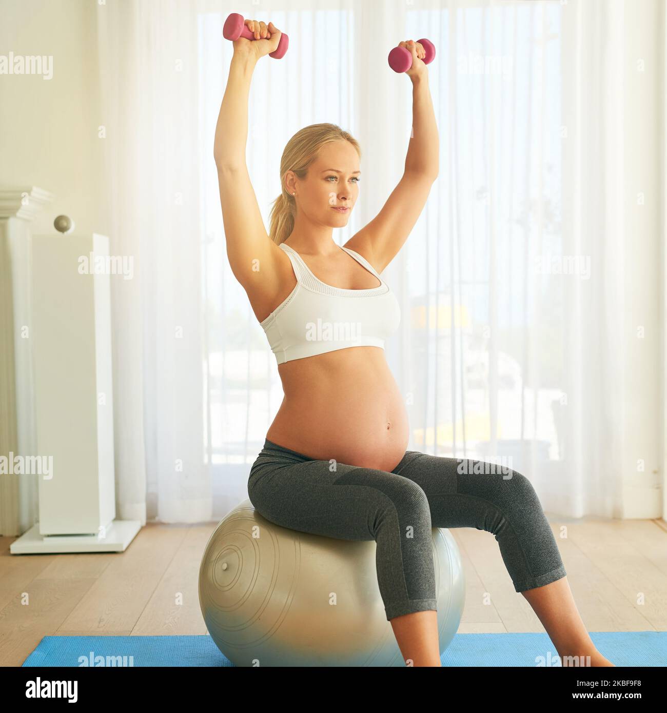 Crescere un bambino sano vale ogni allenamento. Una donna incinta che lavora con una palla da ginnastica e pesi a casa. Foto Stock