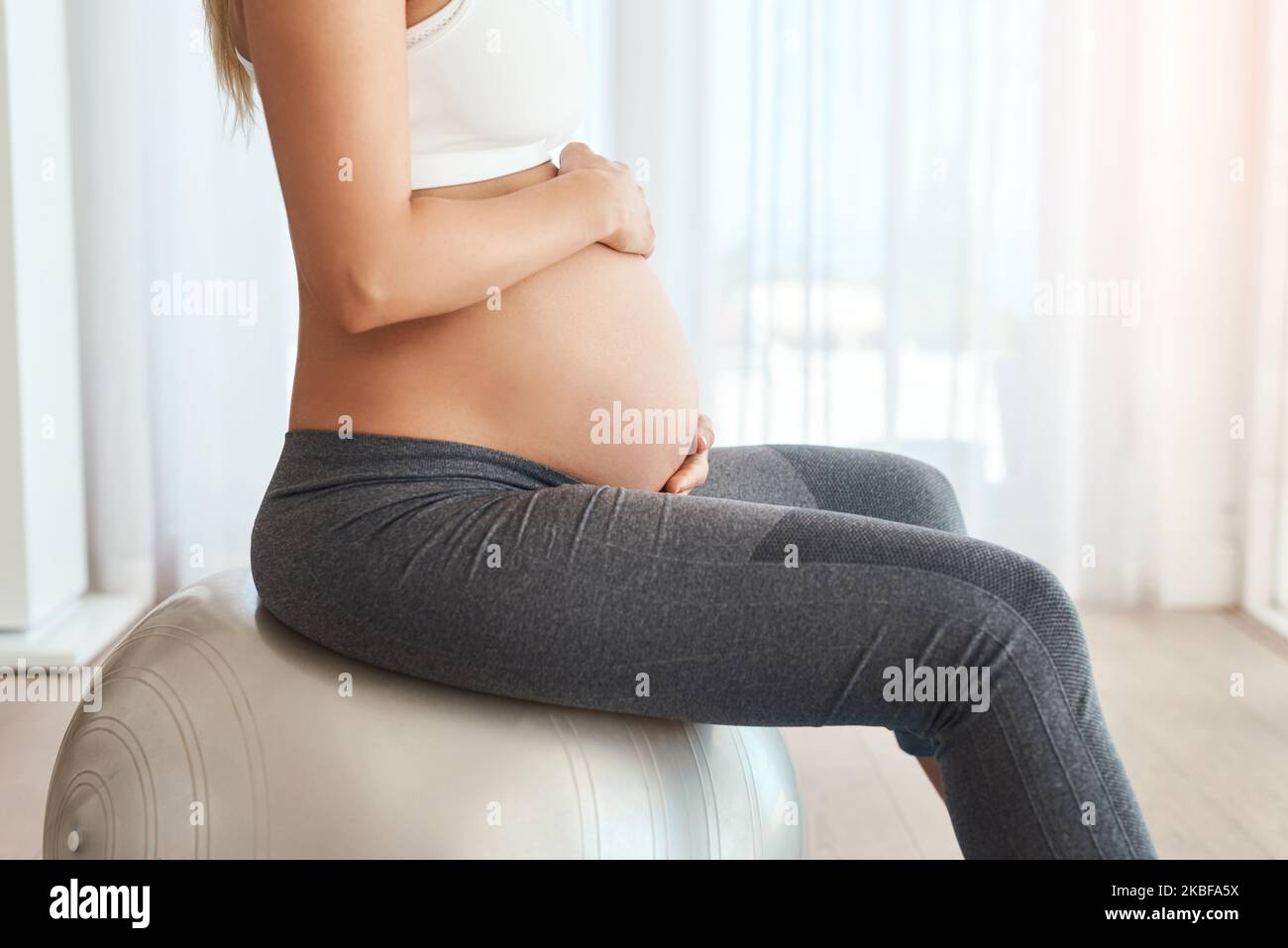 Mantenere il suo corpo forte per la consegna. Corto di una donna incinta che si sta allenando con una palla da ginnastica a casa. Foto Stock