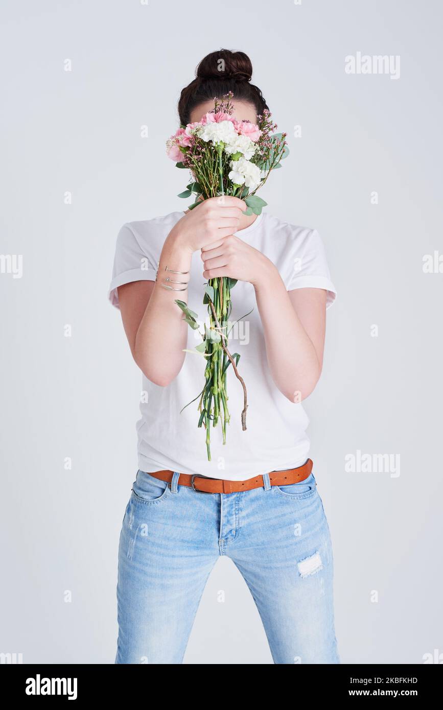 Stare forte ma essere gentile. Studio shot di una donna irriconoscibile che copre il suo volto con fiori su uno sfondo grigio. Foto Stock