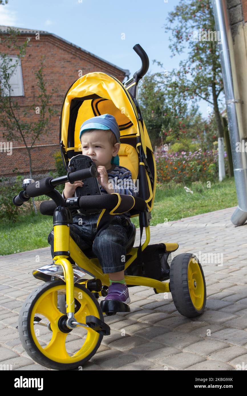 ragazzo seduto su una bicicletta e un triciclo in mano a un'auto Foto Stock