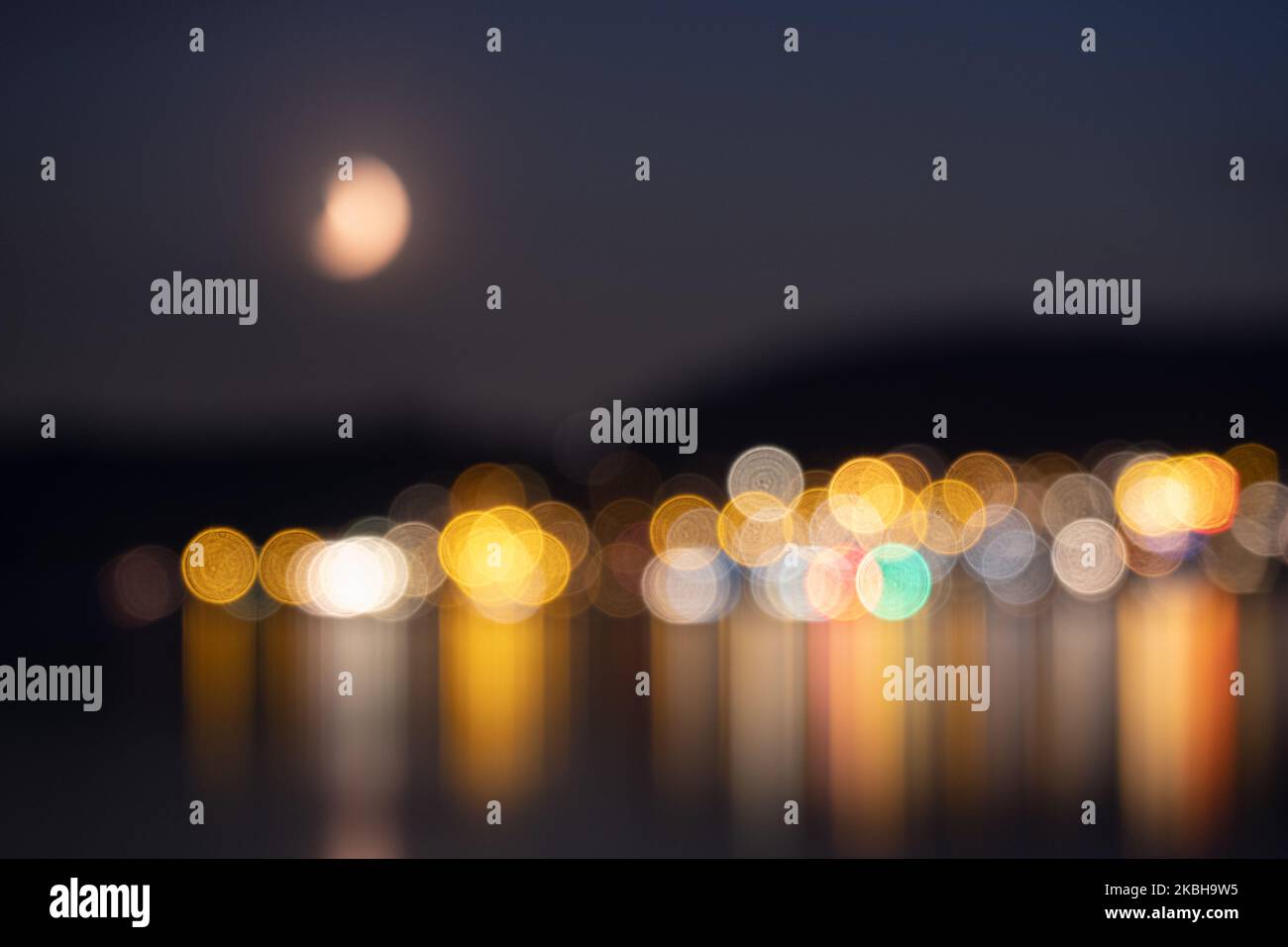 Colorate luci artistiche di una città sul lago insieme alla luna di notte Foto Stock