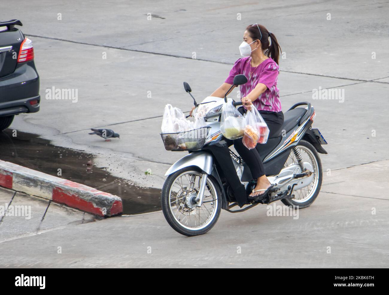 SAMUT PRAKAN, THAILANDIA, 23 2022 SETTEMBRE, Una donna cavalca una moto con acquisti di cibo in sacchetti di plastica Foto Stock