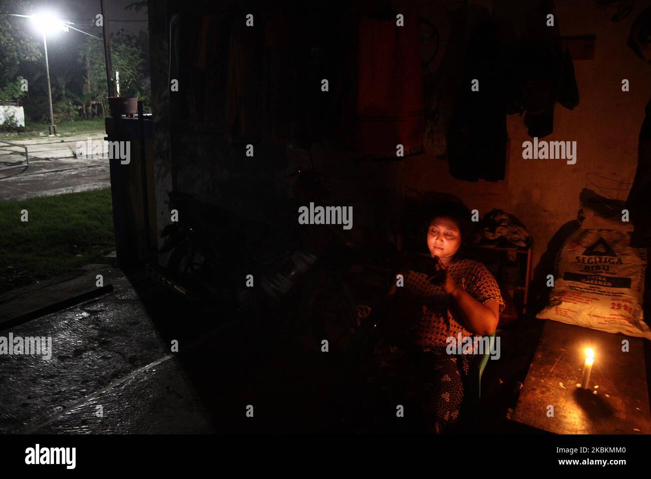 Una donna con smartphone siede sulla terrazza della sua casa illuminata da luci di candela mentre partecipa all'evento Earth Hour 2020 spegnendo le luci elettriche di herr nel villaggio di Wanasari, provincia di Giava Occidentale, Indonesia, il 28 marzo 2020. Earth Hour è un movimento mondiale annuale organizzato dal World Wide Fund for Nature (WWF), che incoraggia gli individui, le comunità e le imprese a spegnere le luci elettriche non essenziali per un'ora, dalle 8:30 alle 9:30 in un giorno specifico alla fine di marzo, come simbolo di impegno per il pianeta. (Foto di Aditya Irawan/NurPhoto) Foto Stock