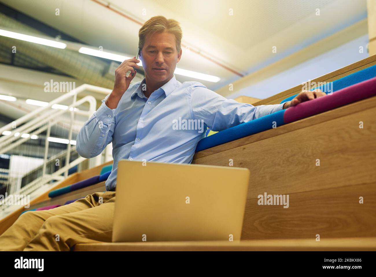 Im guardando i numeri ora. Un uomo d'affari multitasking che risponde al suo cellulare mentre lavora sul suo portatile in ufficio. Foto Stock