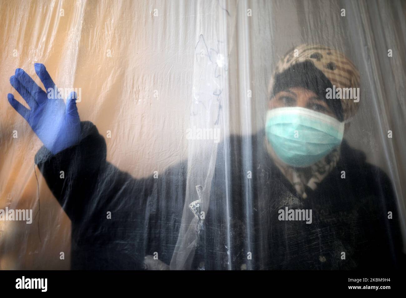 Una donna che indossa una maschera protettiva e un guanto guarda fuori attraverso un foglio di nylon che copre una parte della sua casa a Beit Lahiya, nella striscia di Gaza settentrionale durante la crisi pandemica del coronavirus romanzo, il 11 aprile 2020. (Foto di Majdi Fathi/NurPhoto) Foto Stock