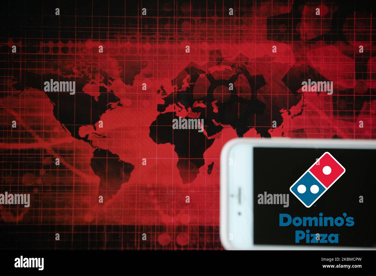 Il logo della consegna di cibo Domino's Pizza è visto su uno schermo di un telefono cellulare accanto a un'illustrazione rossa del mondo e dei mercati finanziari a Francoforte, in Germania, il 14 aprile 2020. È una delle aziende che potrebbero trarre il massimo vantaggio dal blocco. (Foto Illustrazione di Alexander Pohl/NurPhoto) Foto Stock