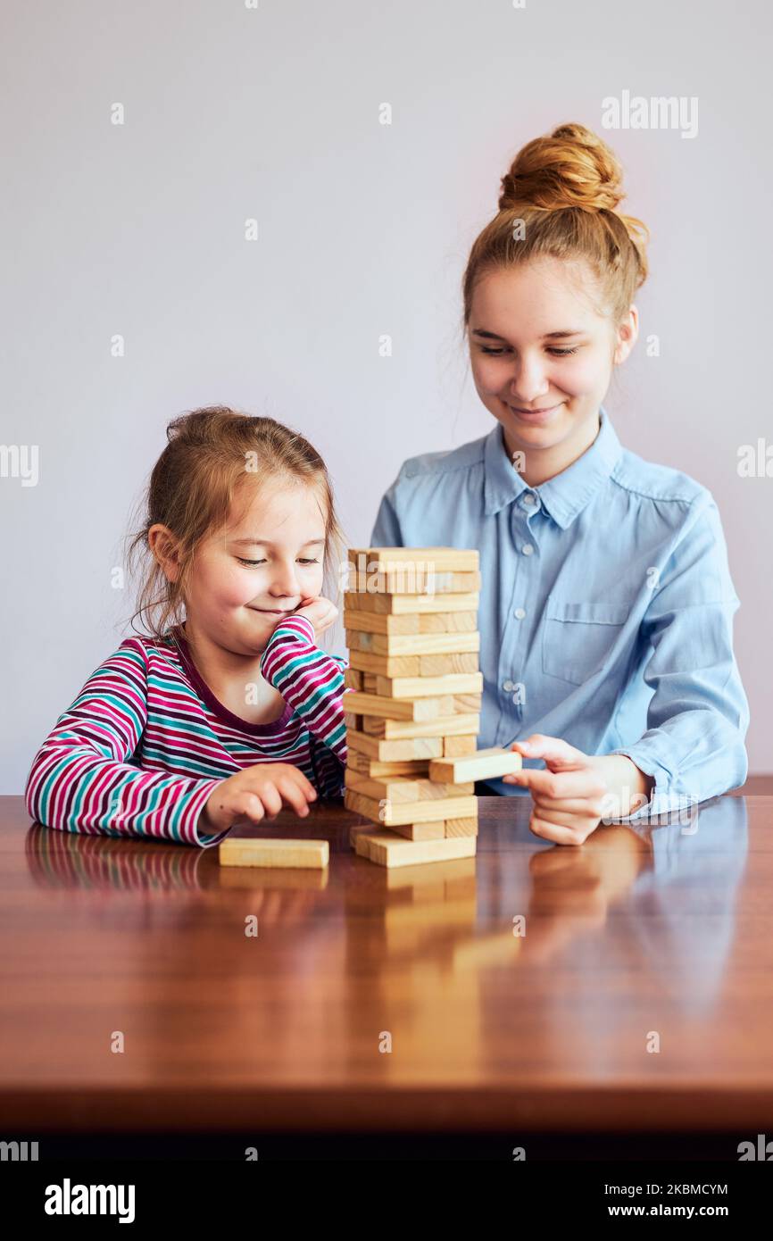 Bambina preschooler e sua sorella maggiore giocando insieme con il gioco blocchi di legno giocattolo. Fratelli che trascorrono del tempo seduti alla scrivania a casa Foto Stock