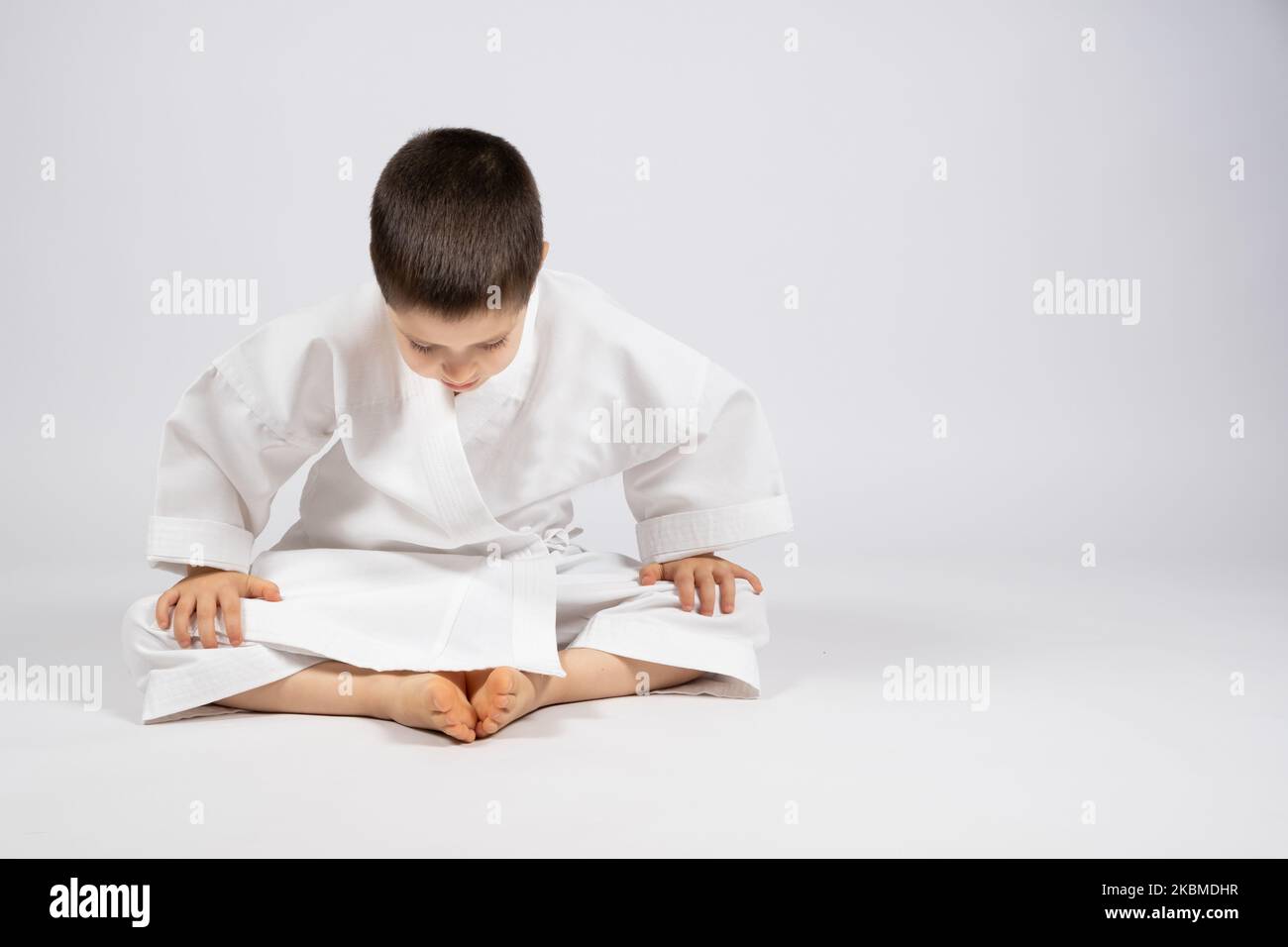 Un ragazzino in un kimono pratica il karate, siede in una posa a farfalla e pratica lo stretching, un posto per il testo. Foto Stock