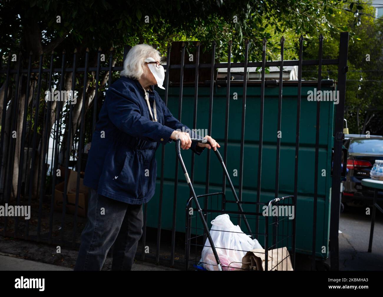 Una donna anziana con una maschera improvvisata per la protezione contro  COVID-19 attende di ricevere un sacchetto di generi alimentari donati dalla  Metro Church nel centro di Santa Monica, CA, USA. La