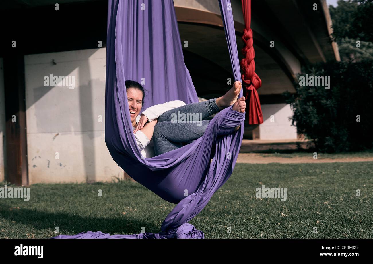 Giovane donna caucasica che si avvolge mentre usa il suo tessuto stretch come amaca appesa su un ponte. Foto Stock