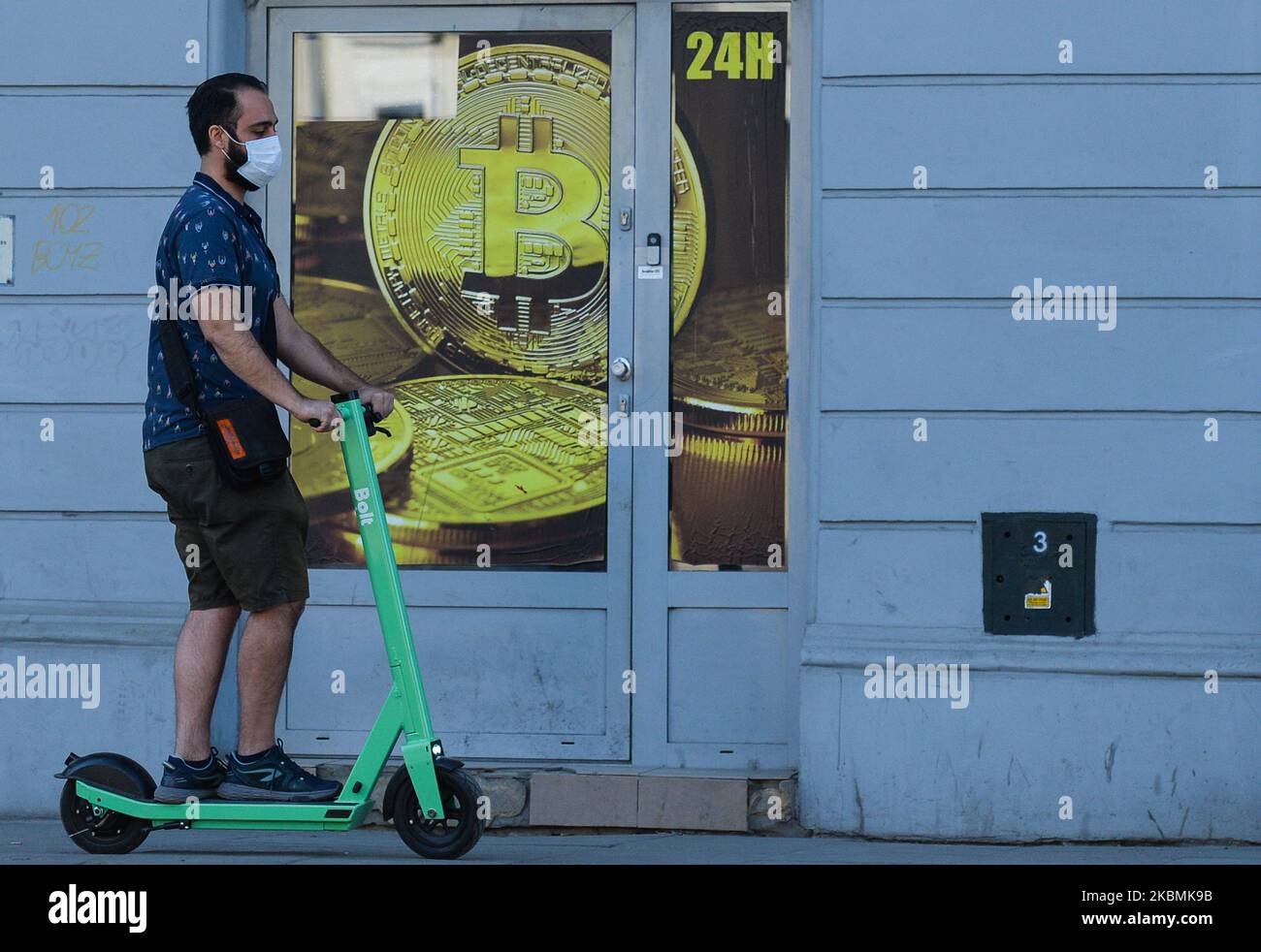 Un uomo che indossa una maschera protettiva guida uno scooter elettrico di fronte a un negozio di scambio Bitcoin nel centro della città di Cracovia. Sabato 18 aprile 2020 a Cracovia, Polonia. (Foto di Artur Widak/NurPhoto) Foto Stock