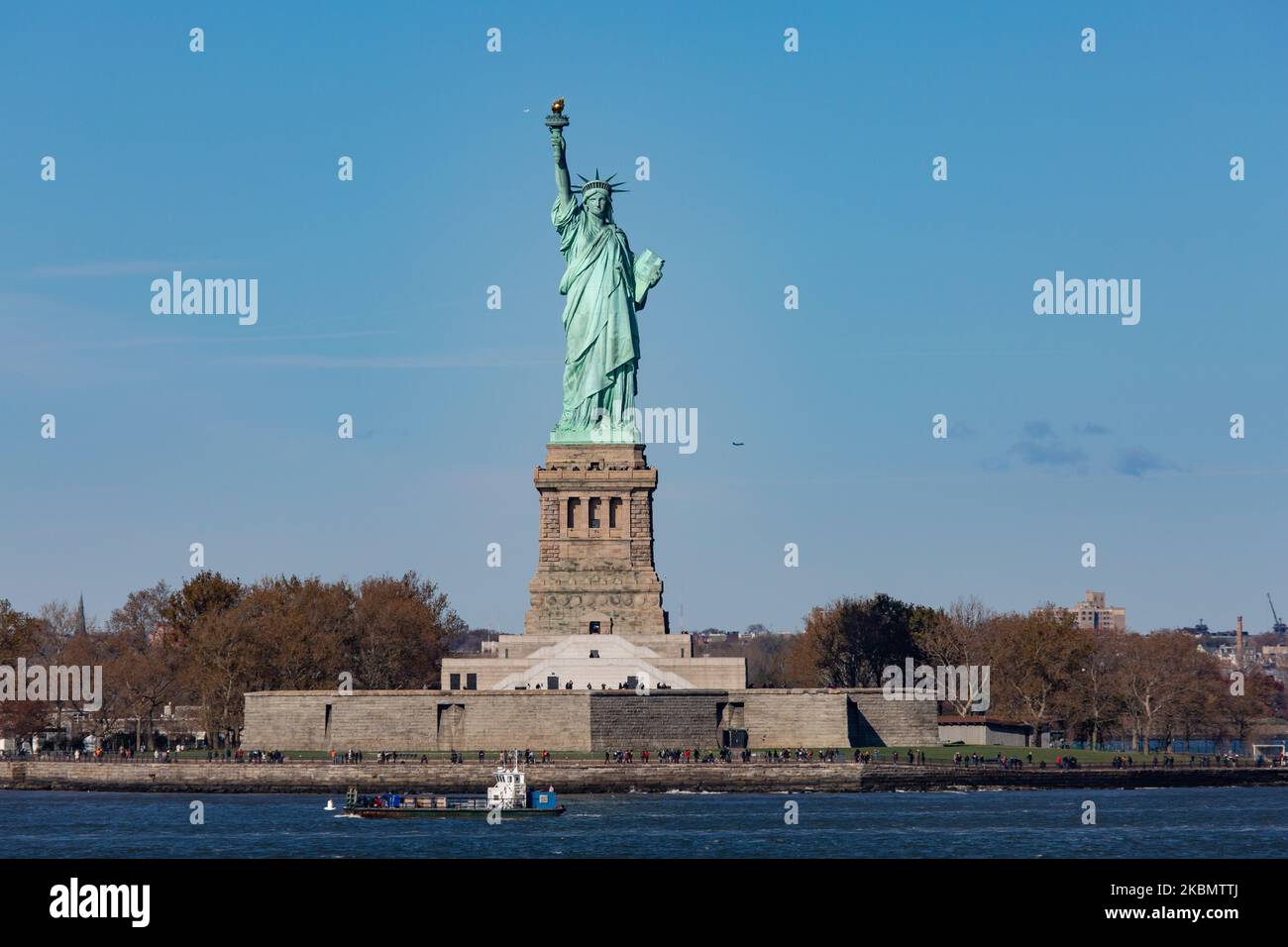 Statua della libertà come si vede durante una giornata senza nuvole cielo blu e un aereo Delta Air Lines che vola dietro. La statua ha turisti e visitatori a Liberty Island Manhattan, New York City, Stati Uniti, da un traghetto in mare. L'iconica statua in rame raggiunge i 93m metri sopra il mare ed è stata dedicata il 28 ottobre 1886. Fu progettata dallo scultore francese Frédéric Auguste Bartholdi e la sua struttura metallica fu costruita da Gustave Eiffel, la scultura fu un dono del popolo francese. Oggi è una popolare attrazione turistica, una destinazione di viaggio, punto di riferimento per NYC e gli Stati Uniti uno dei più reco Foto Stock