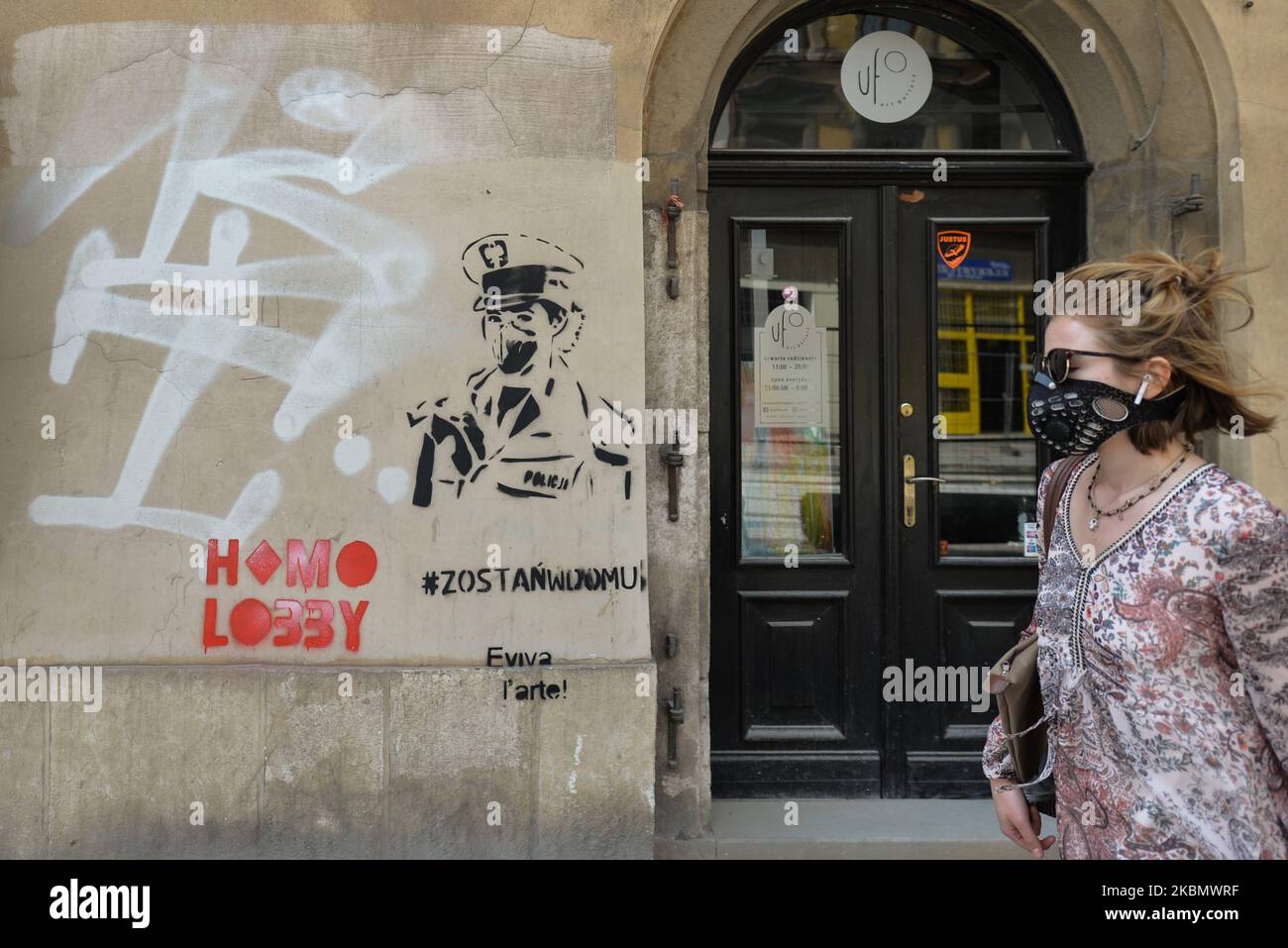 Una donna che indossa una maschera protettiva passa davanti ai graffiti "Stay at Home" visti su un muro a Cracovia, quartiere Kazimierz. Venerdì 24 aprile 2020 a Cracovia, Polonia. (Foto di Artur Widak/NurPhoto) Foto Stock