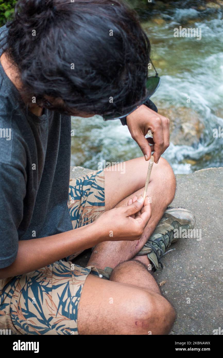 Luglio 14th 2022, Himachal Pradesh India.. Una posa laterale di un giovane uomo con un ragazzo che rotola un'articolazione di erbacce sulle colline dell'Himalaya. Foto Stock