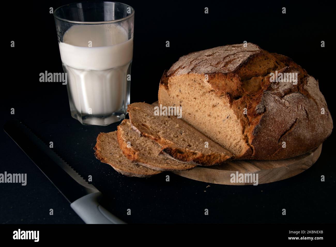 foto del pane fresco affettato su un tavolo da cucina in legno con un bicchiere di latte Foto Stock