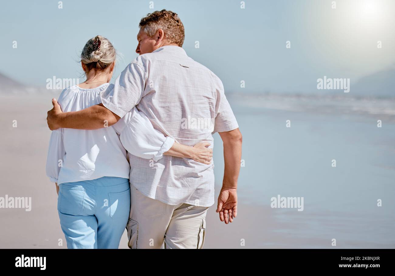 Amore, coppia anziana e spiaggia per camminare, vacanza e felice di essere amorevole insieme, viaggio o abbraccio. Romanticismo, uomo maturo e donna anziana abbracciano Foto Stock