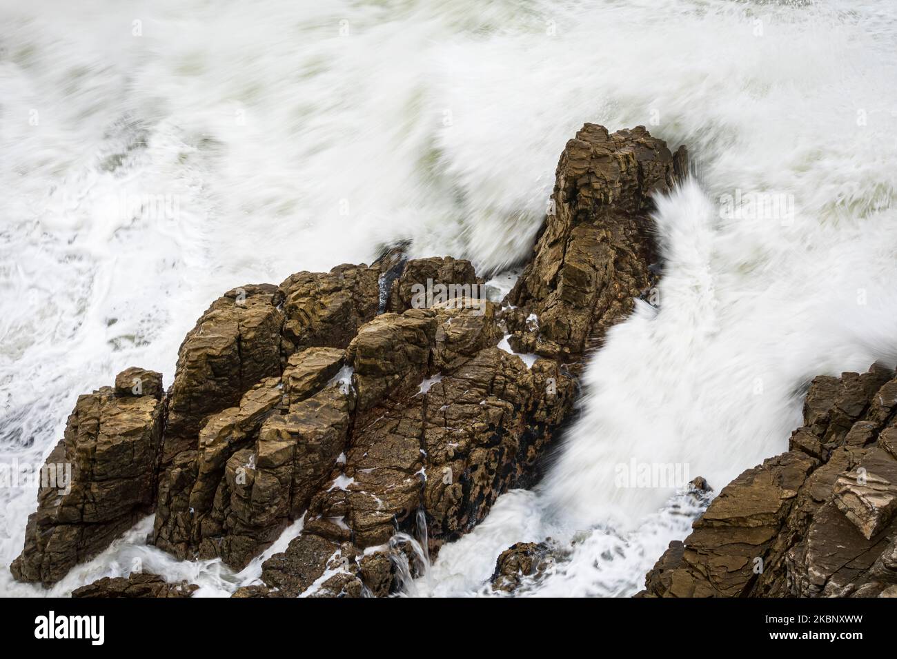 Una potente onda oceanica si schianta contro rocce aspre lungo la panoramica costa di Hermanus in Sud Africa, mostrando la bellezza e la forza della natura. Foto Stock