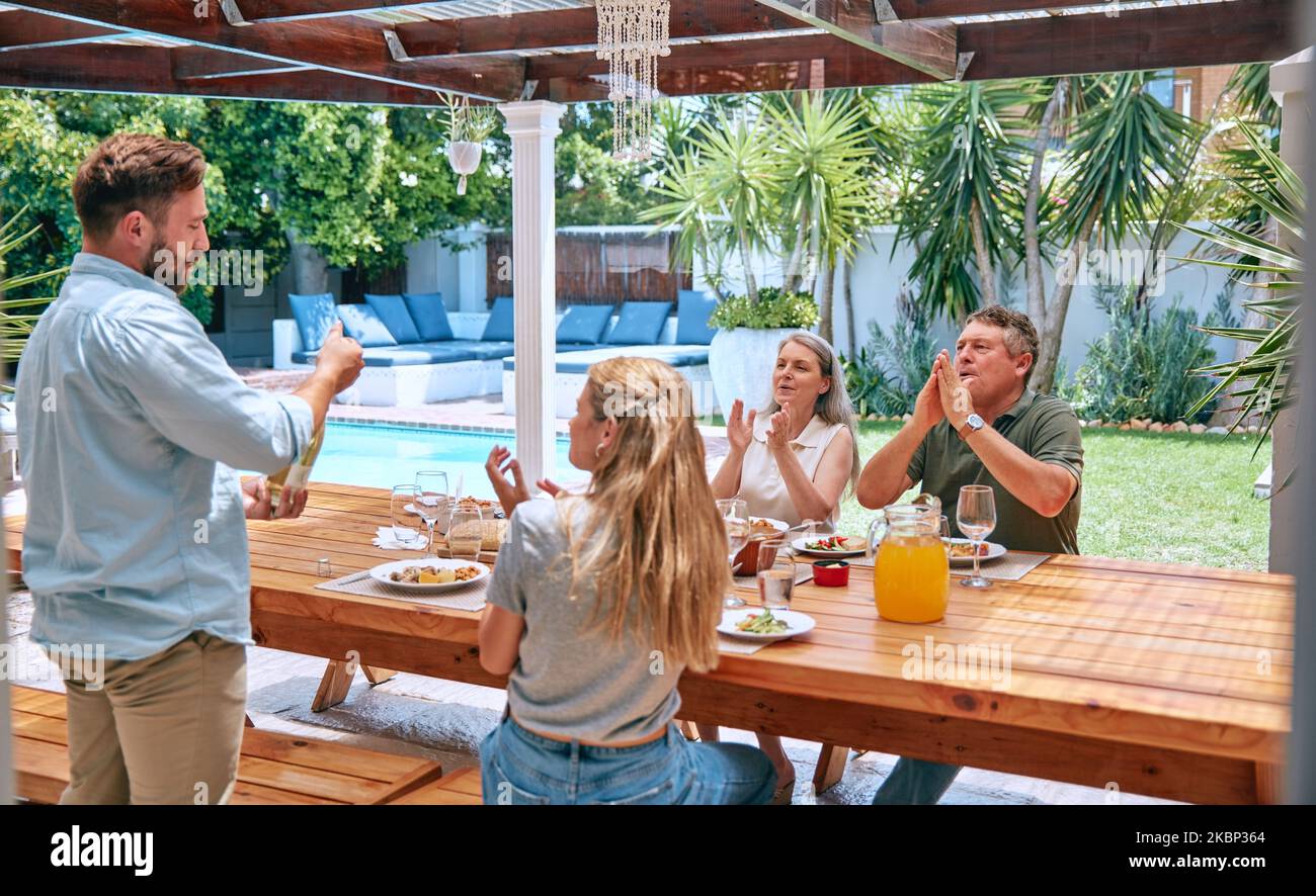 Champagne, festa e famiglia con applausi a pranzo partito con cibo, amore e relax nel giardino di casa. Vino, felice e uomo con alcol a. Foto Stock