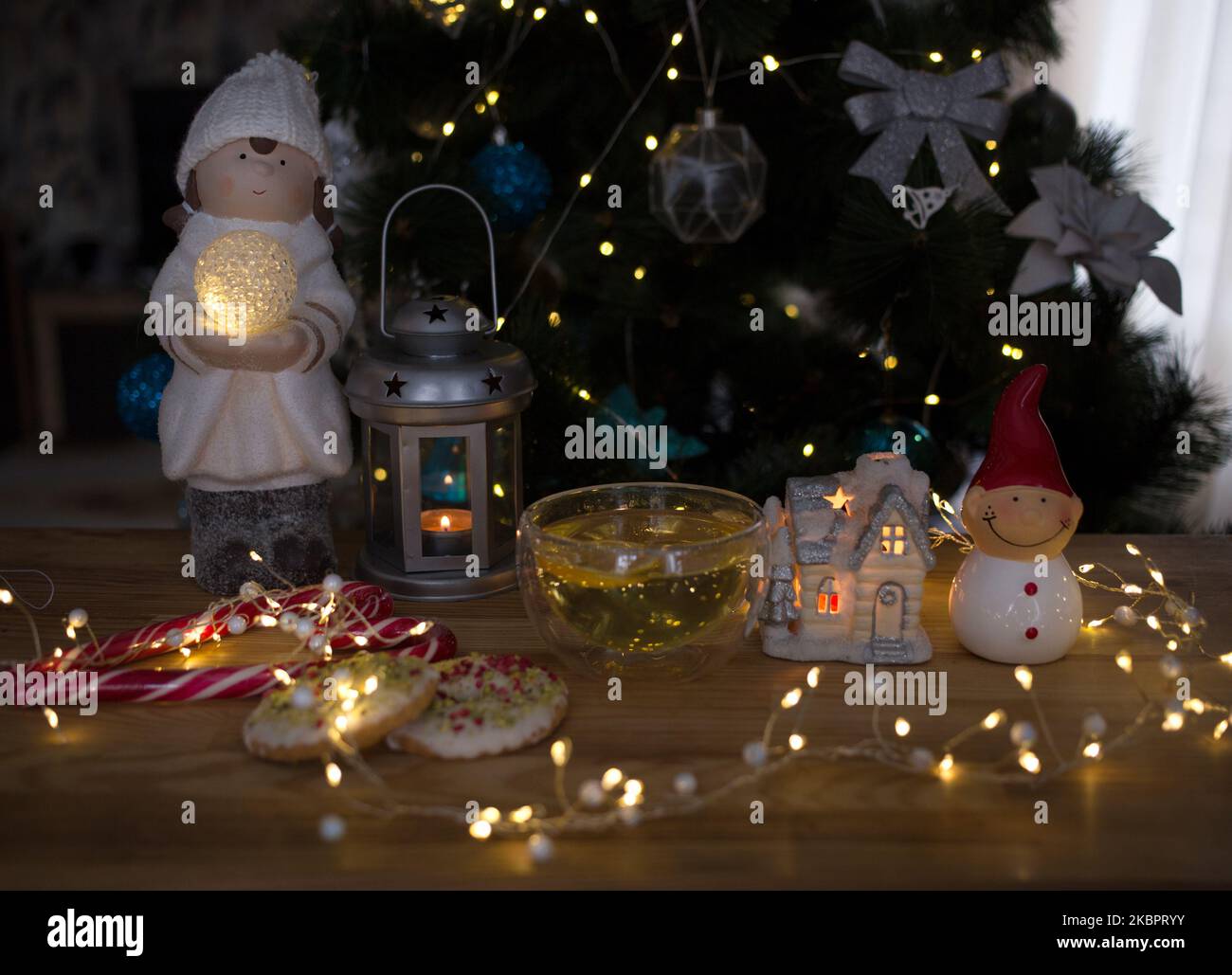 Accogliente foto d'atmosfera su un tema natalizio. Una tazza trasparente con tè, un riflesso delle luci di un ghirlaio in esso contenuto. Pupazzo di neve ricordo, biscotti, lan Foto Stock