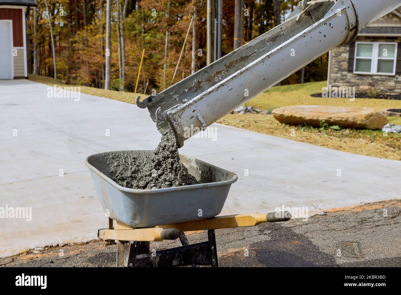 Il betoniera versa il cemento bagnato nella carriola durante la costruzione in cantiere Foto Stock