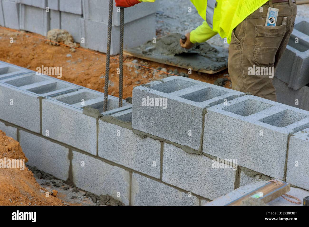 Muratore di costruzione di muratore sta posando giù un'altra fila di blocchi di cemento in luogo di costruzione Foto Stock