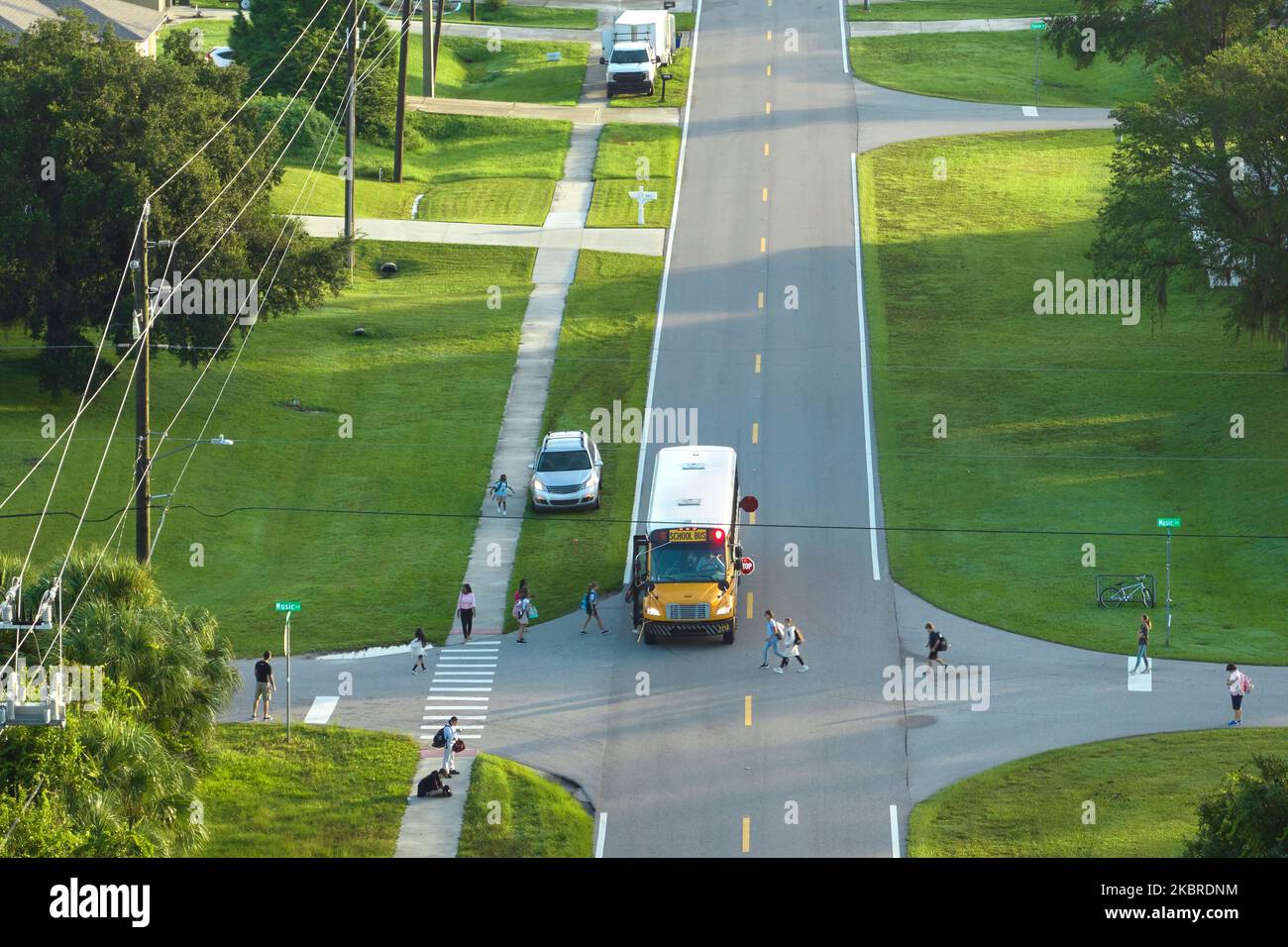 Veduta aerea dell'autobus americano giallo scuola che raccoglie i bambini alla fermata dell'autobus marciapiede per i loro lessong in prima mattina. Trasporto pubblico nel Foto Stock