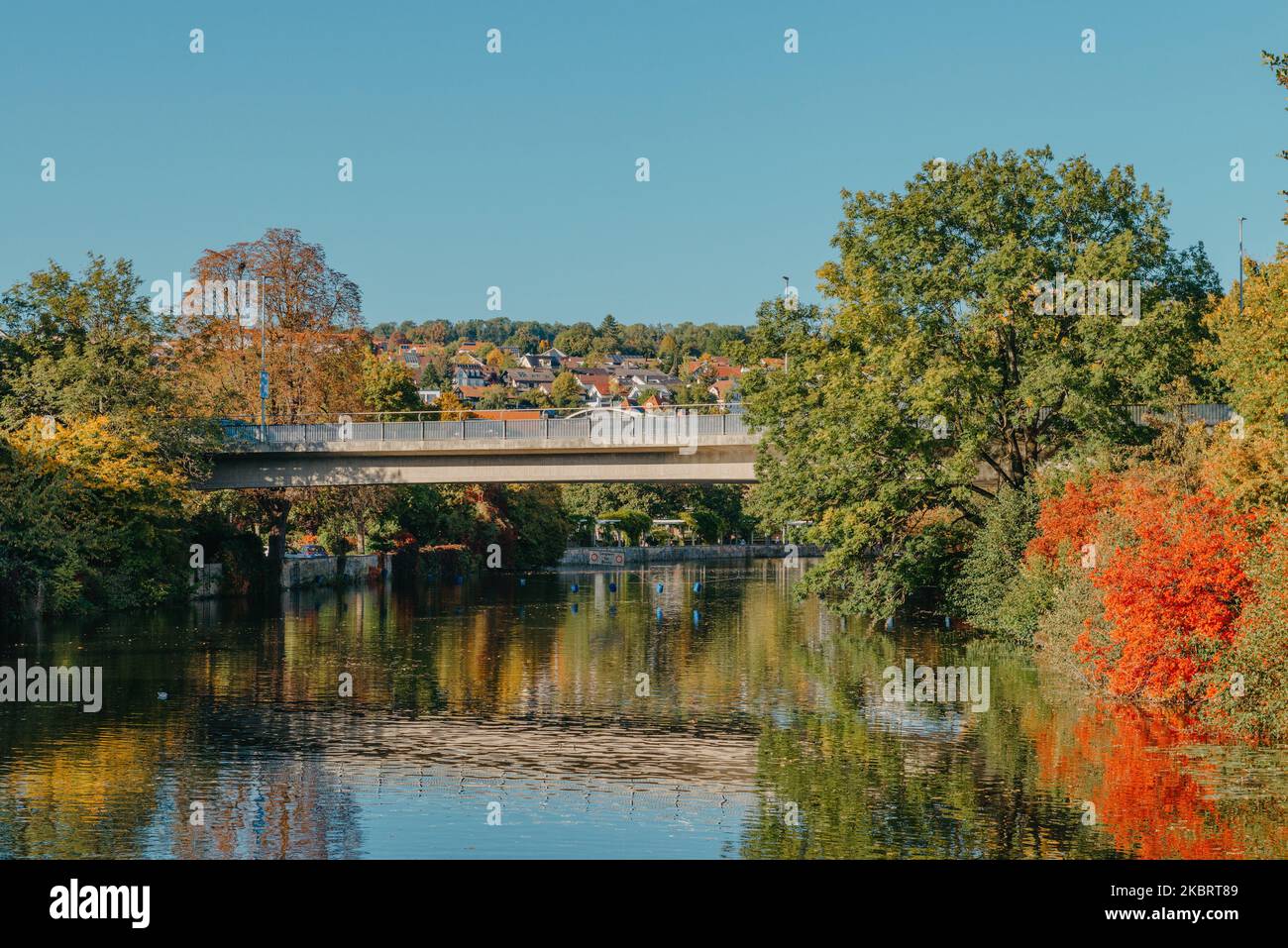 Bel piccolo fiume con acqua pulita e limpida davanti di colorati alberi autunnali e piccola città vecchia sulla collina agaista bel cielo blu e nuvole durante Foto Stock