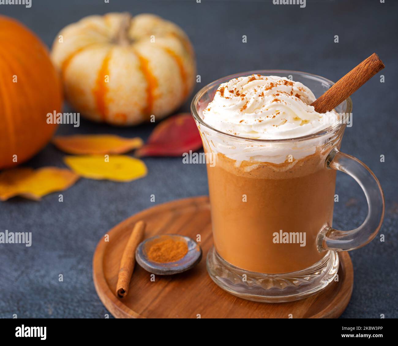 Latte di spezie di zucca con panna montata in una tazza di vetro in un piatto di legno Foto Stock